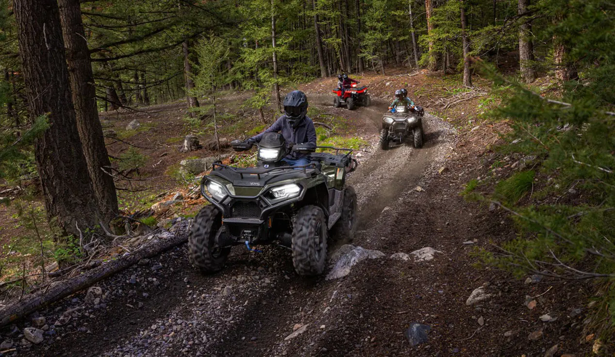 3 Polaris Sportsman ATVs driving on a forest trail.