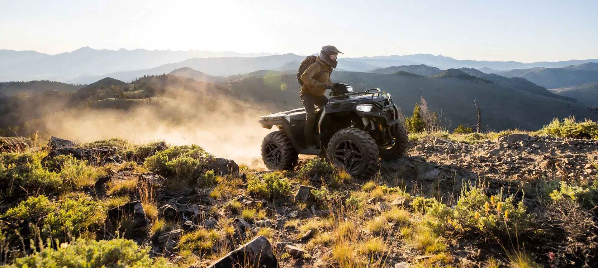 A rider on a Polaris Sportsman 600 ATV climbing over rocky terrain on a hill.