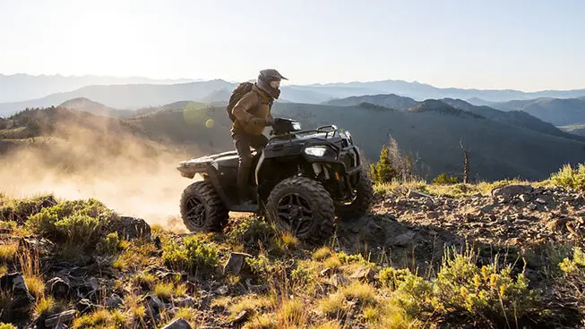 A rider on a Polaris Sportsman 600 ATV climbing over rocky terrain on a hill.