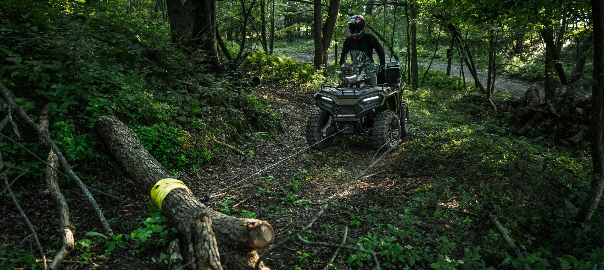 Rider on a Polaris Sportsman 600 ATV using a winch to move a log in the forest.
