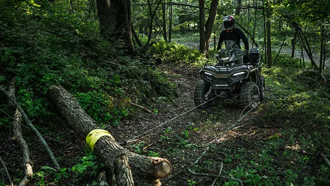 Rider on a Polaris Sportsman 600 ATV using a winch to move a log in the forest.