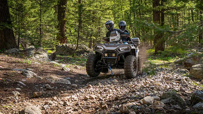 2 riders on a Polaris Sportsman 600 Touring ATV driving through the forest.