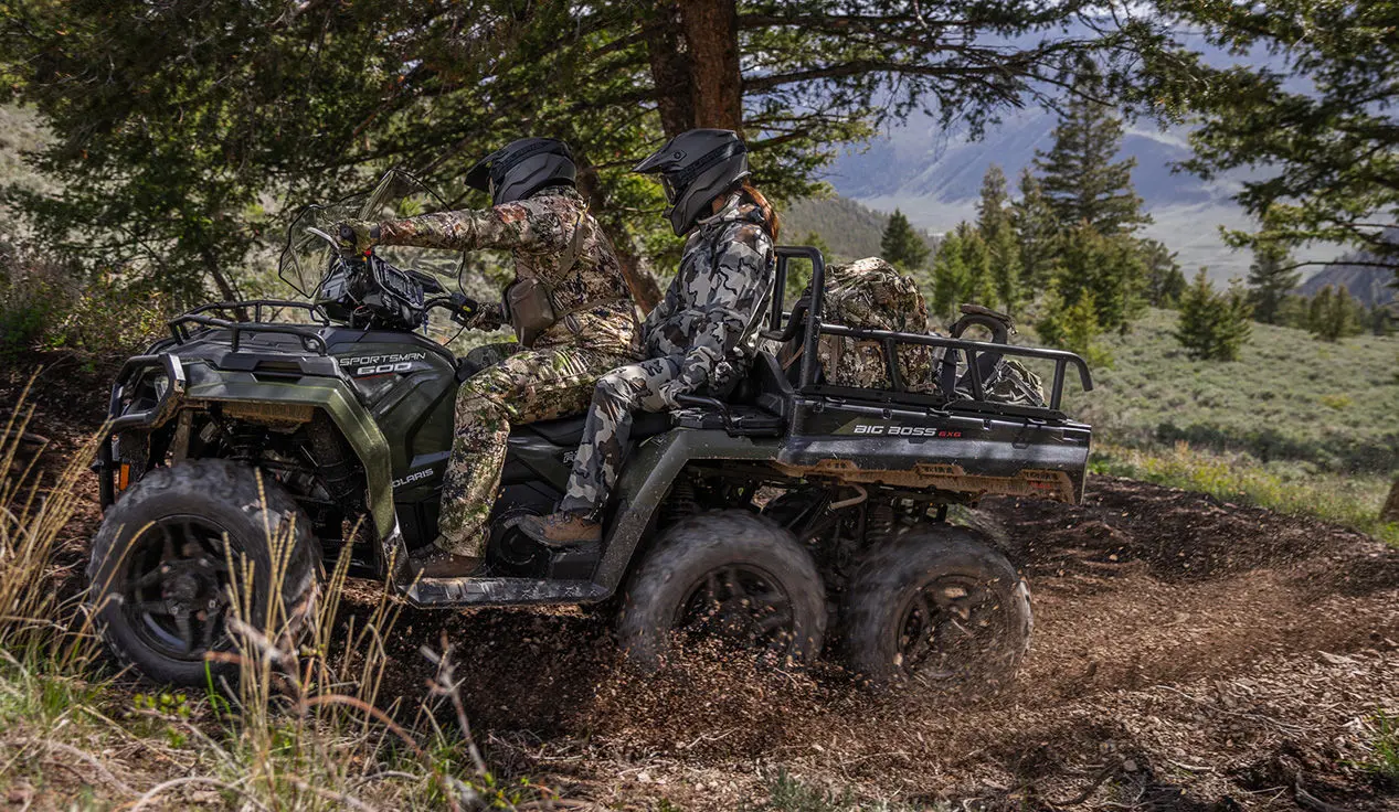Two hunters riding on a Polaris Sportsman 6x6 600 ATV through mud.