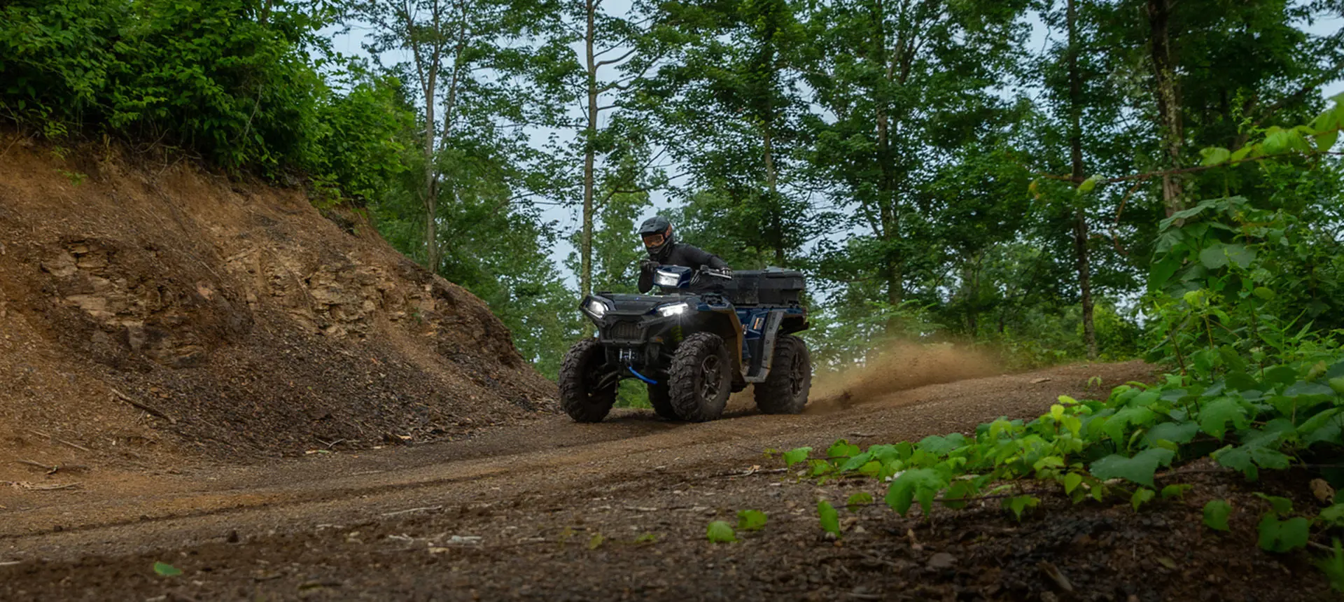 A rider on a Polaris Sportsman 850 ATV driving down a dirt road trail.