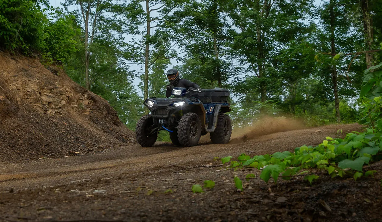 A rider on a Polaris Sportsman 850 ATV driving down a dirt road trail.