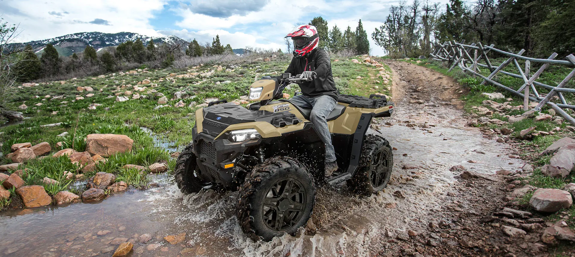 A rider on a Polaris Sportsman 850 ATV driving through a shallow ravine.