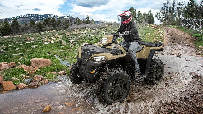 A rider on a Polaris Sportsman 850 ATV driving through a shallow ravine.