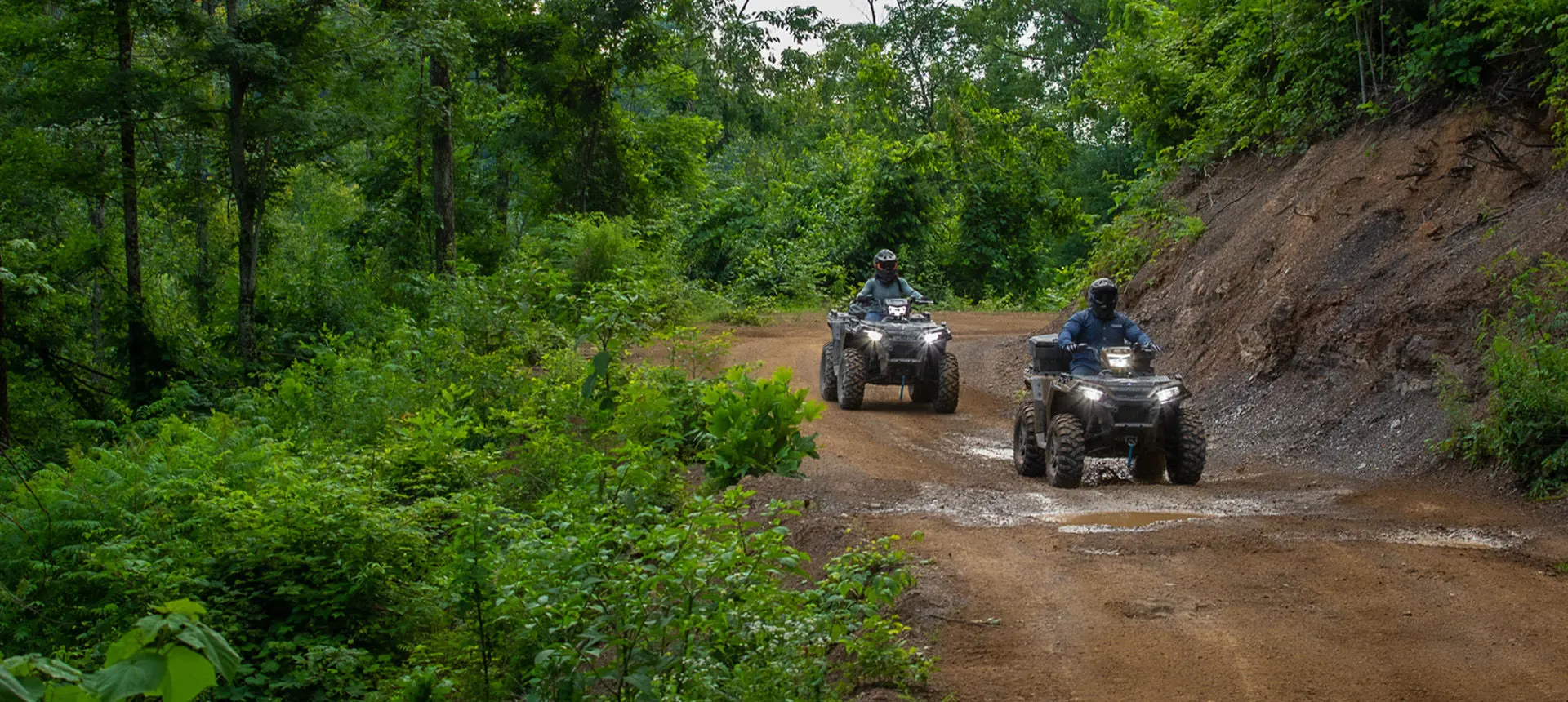 Two Polaris Sportsman 850 ATVs driving on a forest trail.