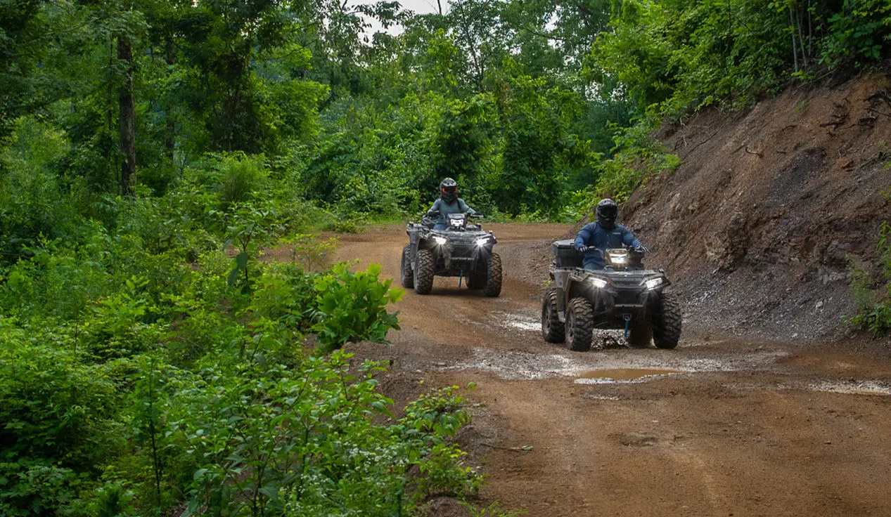 Two Polaris Sportsman 850 ATVs driving on a forest trail.