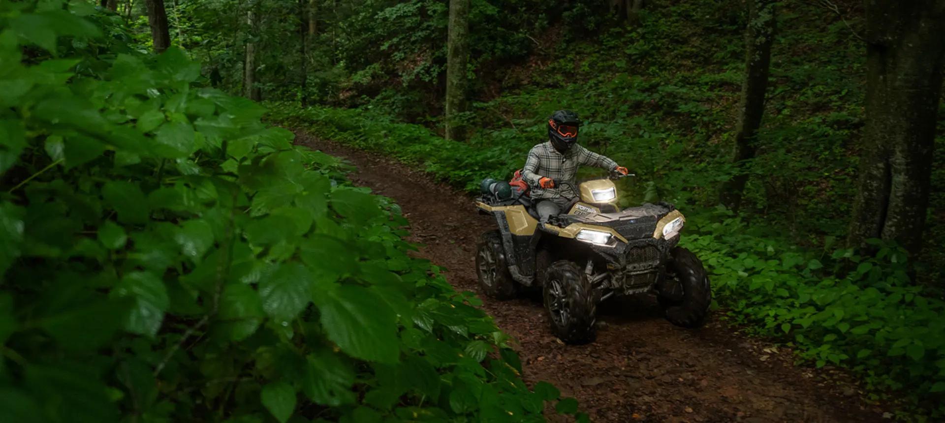 A rider on a Polaris Sportsman 850 ATV trail riding in the forest.