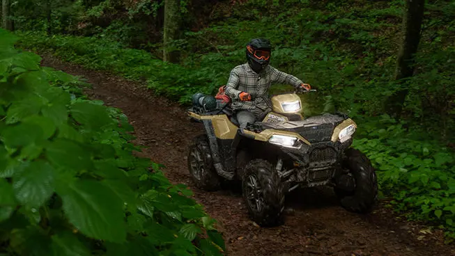 A rider on a Polaris Sportsman 850 ATV trail riding in the forest.