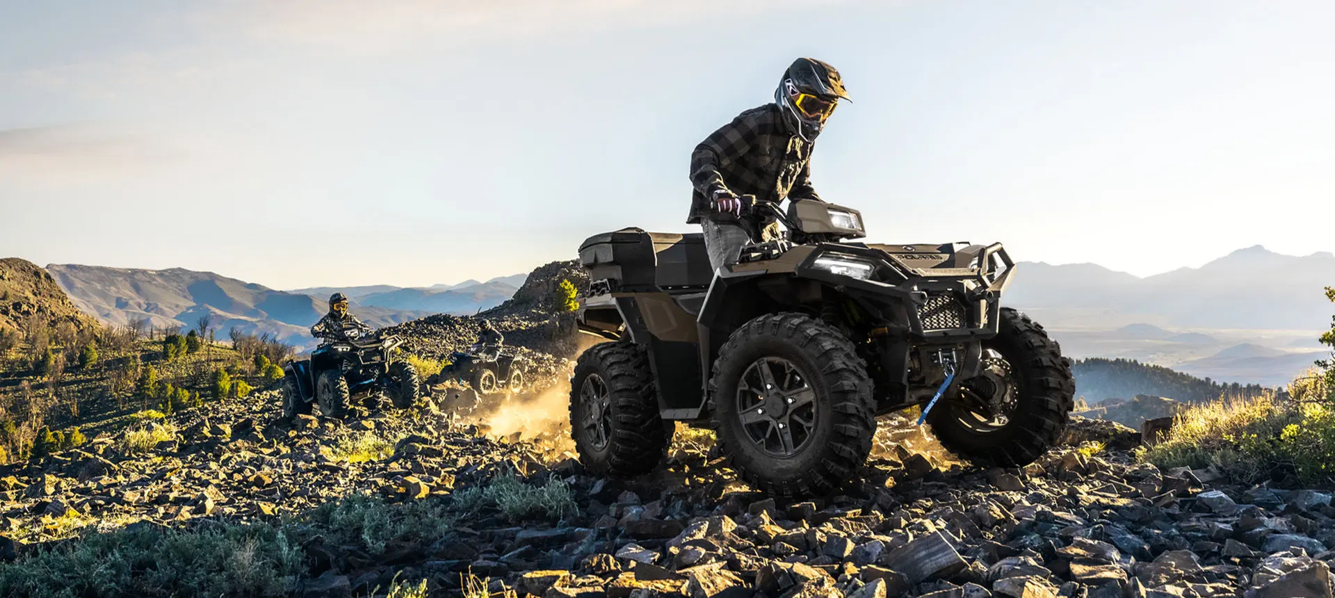 2 Polaris Sportsman 850 ATVs driving over rocky terrain on a hill.
