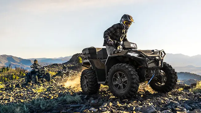 2 Polaris Sportsman 850 ATVs driving over rocky terrain on a hill.