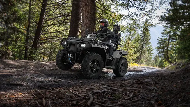 2 riders on a Polaris Sportsman Touring XP 1000 Trail ATV driving on a forest trail.