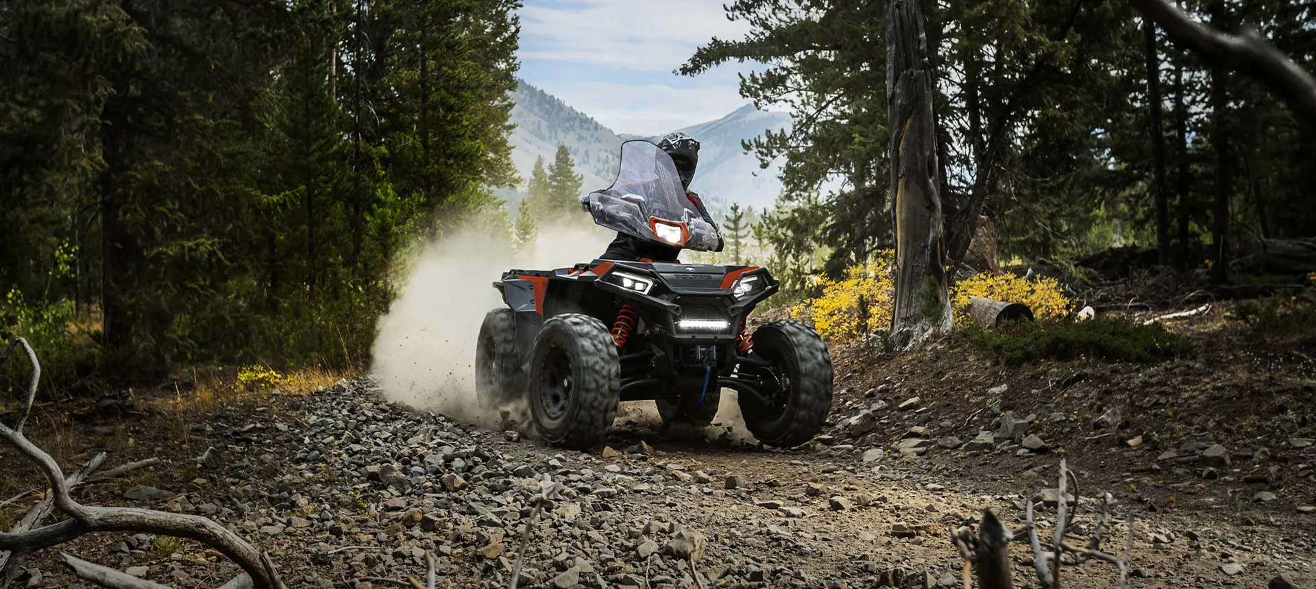 A rider on a Polaris Sportsman XP 1000 S ATV taking a tight corner on a rocky forest trail.
