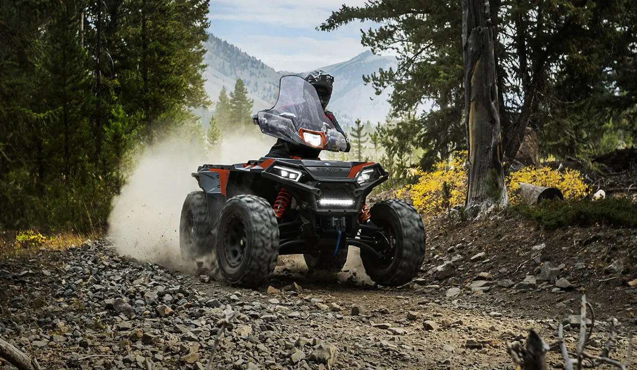 A rider on a Polaris Sportsman XP 1000 S ATV taking a tight corner on a rocky forest trail.
