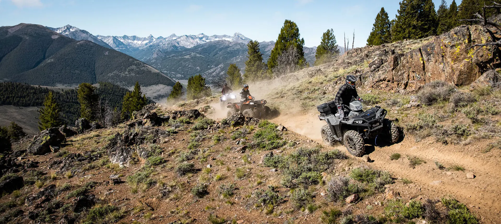 3 Polaris Sportsman XP 1000 S ATVs driving on a trail in the mountains.