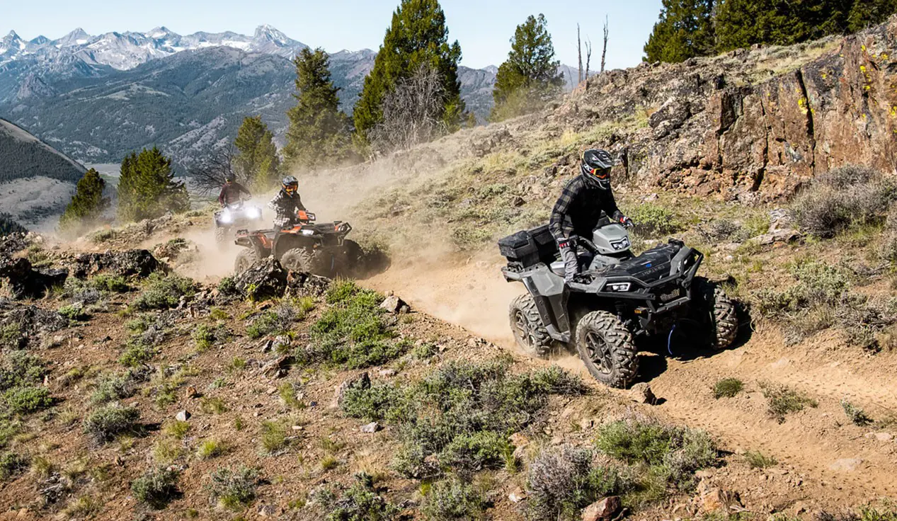 3 Polaris Sportsman XP 1000 S ATVs driving on a trail in the mountains.