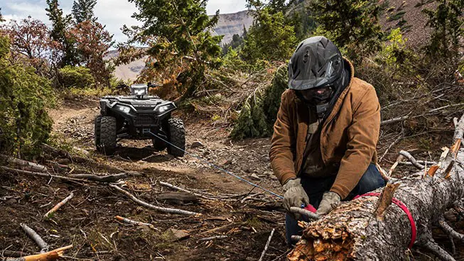 A person using the winch from their Polaris Sportsman XP 1000 ATV to move a log off the trail.