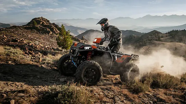 Side profile of a rider on a Polaris Sportsman XP 1000 S ATV ascending a hill.