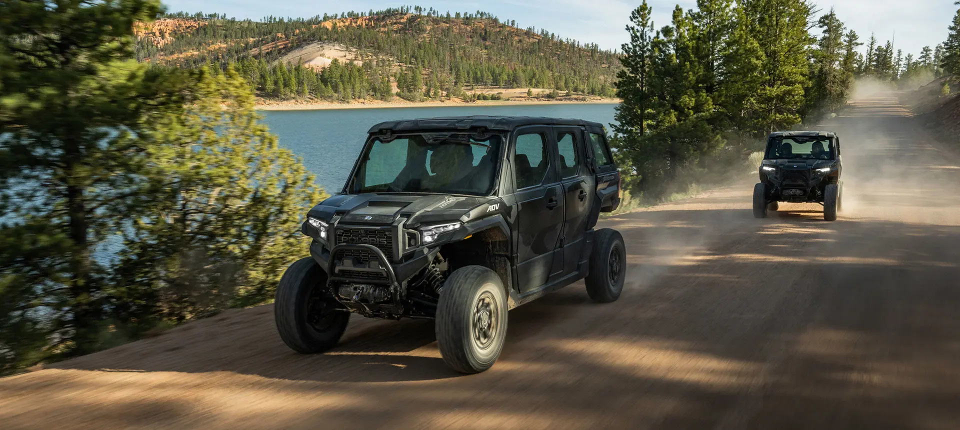 Two Polaris XPEDITION ADV 5 NorthStar side-by-sides cruising down a trail near a lake.