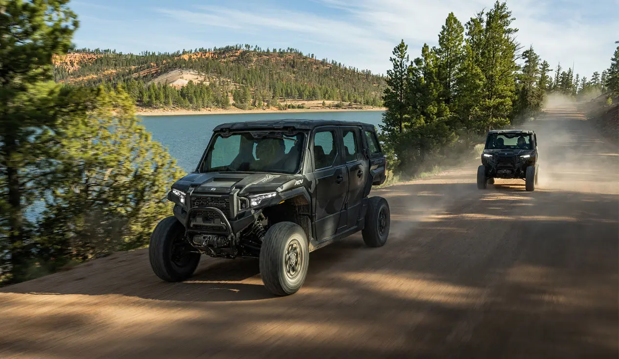 Two Polaris XPEDITION ADV 5 NorthStar side-by-sides cruising down a trail near a lake.