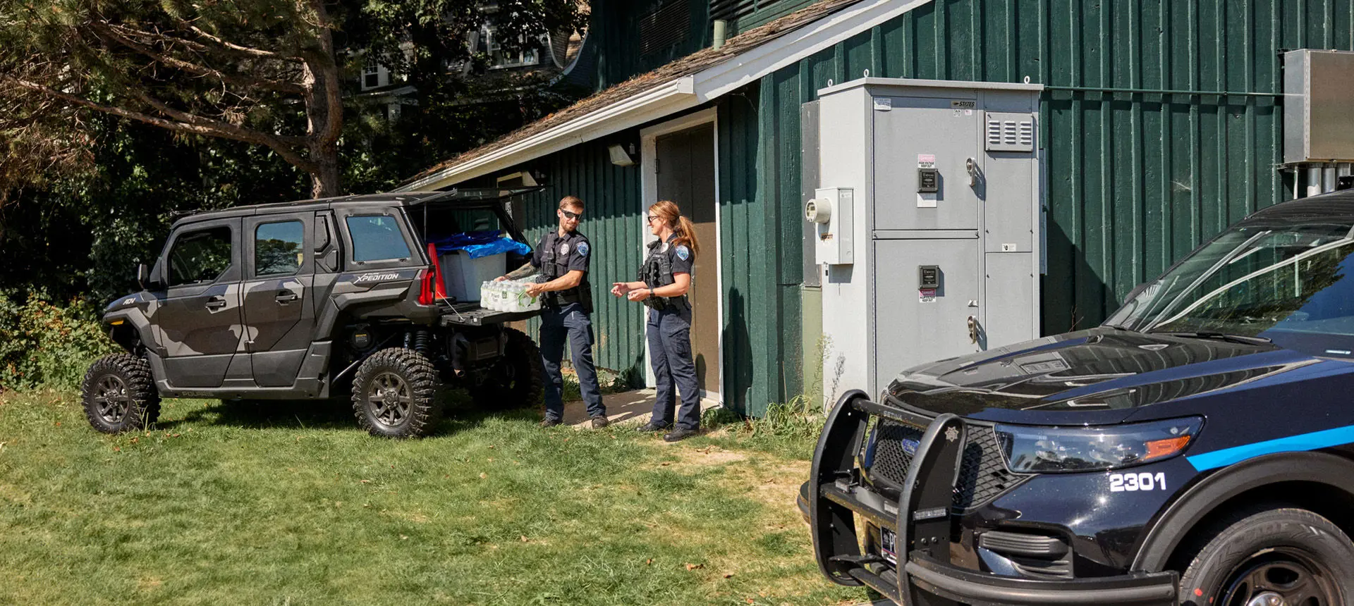 2 law enforcement officers unloading water from the cargo box of a Polaris XPEDITION ADV 5 NorthStar side-by-side.