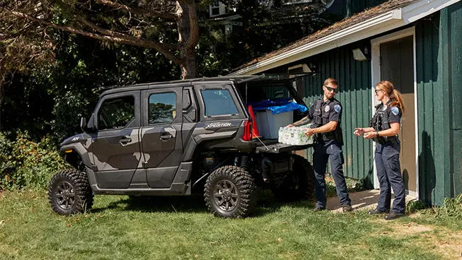 2 law enforcement officers unloading water from the cargo box of a Polaris XPEDITION ADV 5 NorthStar side-by-side.