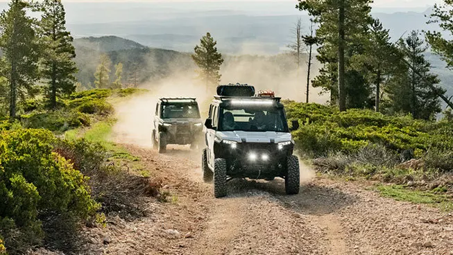 Two Polaris XPEDITION XP NorthStar side-by-side cruising on a dirt road.
