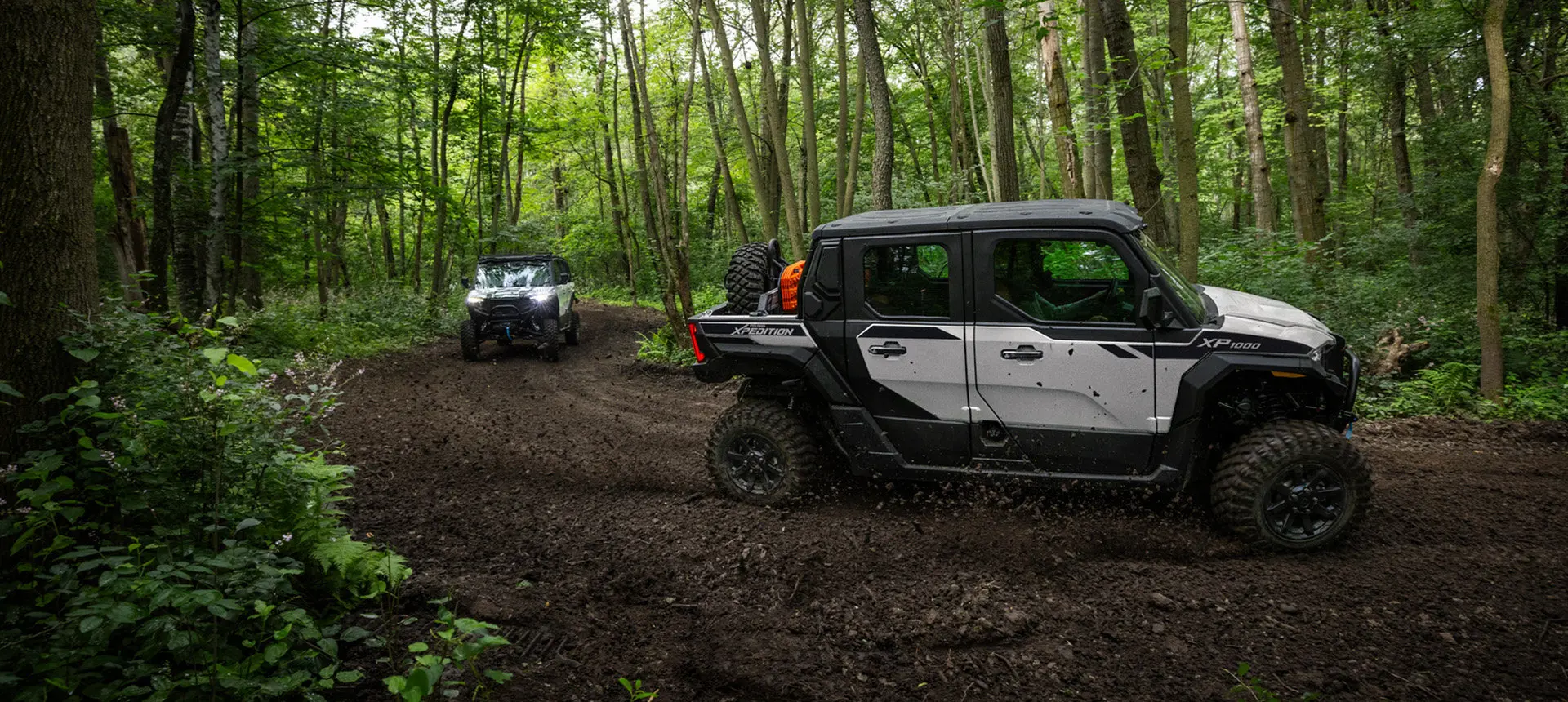 Two Polaris XPEDITION XP NorthStar side-by-sides driving on a trail deep in the forest.