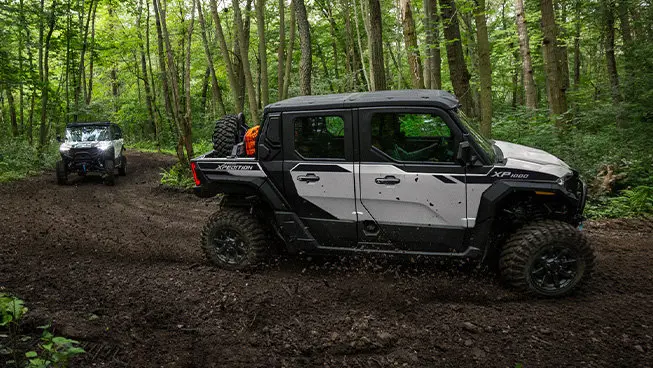 Two Polaris XPEDITION XP NorthStar side-by-sides driving on a trail deep in the forest.