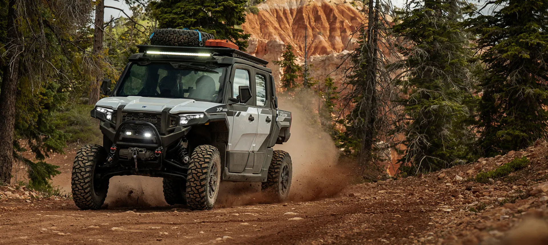 Front-end view of a Polaris XPEDITION XP NorthStar side-by-side with headlights illuminated on a trail.
