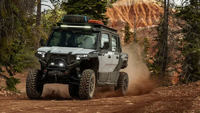 Front-end view of a Polaris XPEDITION XP NorthStar side-by-side with headlights illuminated on a trail.