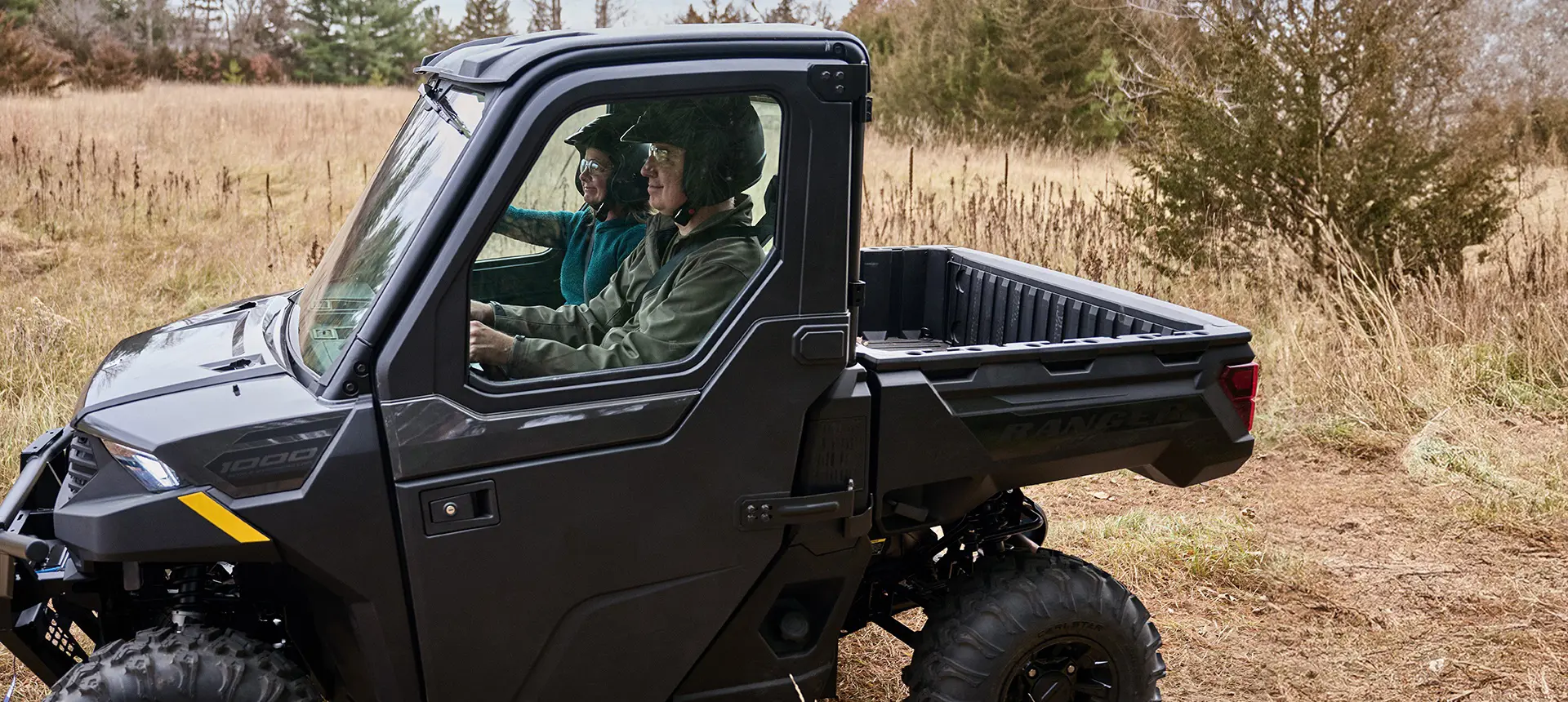Side profile of 2 riders in a Polaris RANGER 1000 CAB UTV.