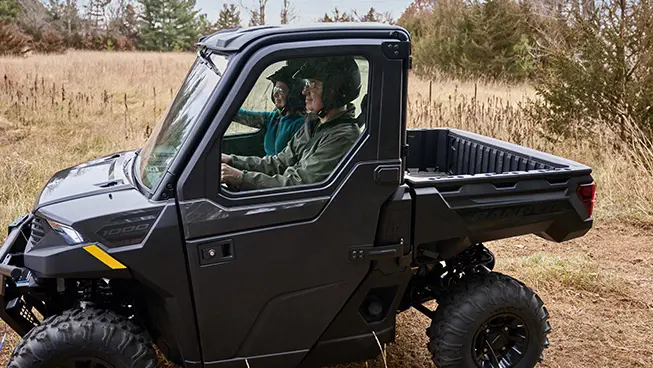 Side profile of 2 riders in a Polaris RANGER 1000 CAB UTV.