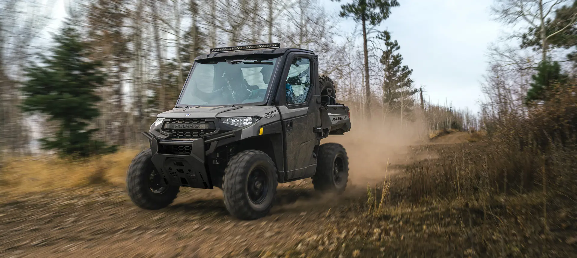 A Polaris RANGER XP 1000 NorthStar Edition UTV with a lightbar installed driving down a trail.