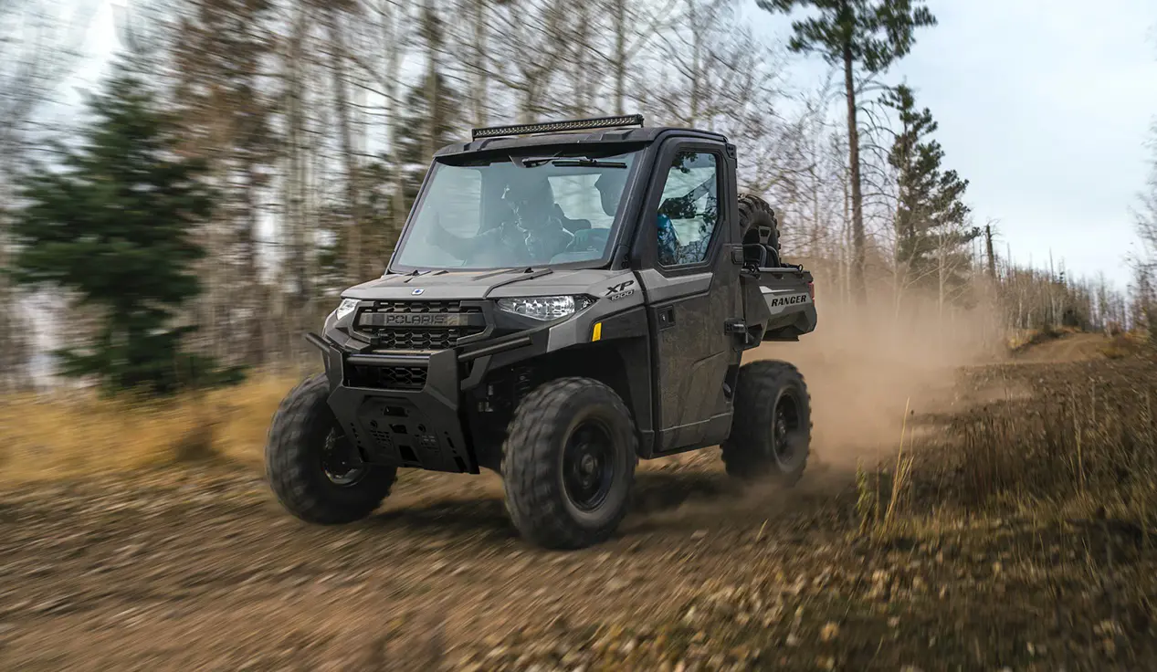 A Polaris RANGER XP 1000 NorthStar Edition UTV with a lightbar installed driving down a trail.