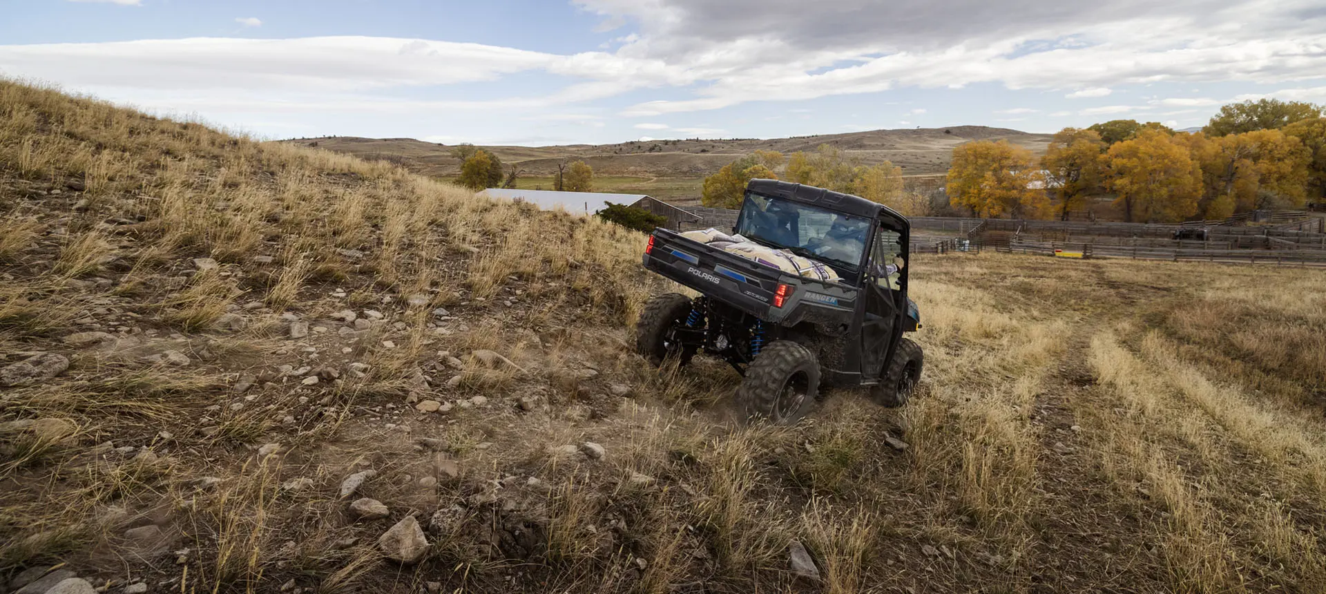 Rear view of a Polaris RANGER XP Kinetic electric UTV with a fully loaded cargo box driving through a field.