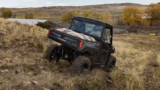 Rear view of a Polaris RANGER XP Kinetic electric UTV with a fully loaded cargo box driving through a field.