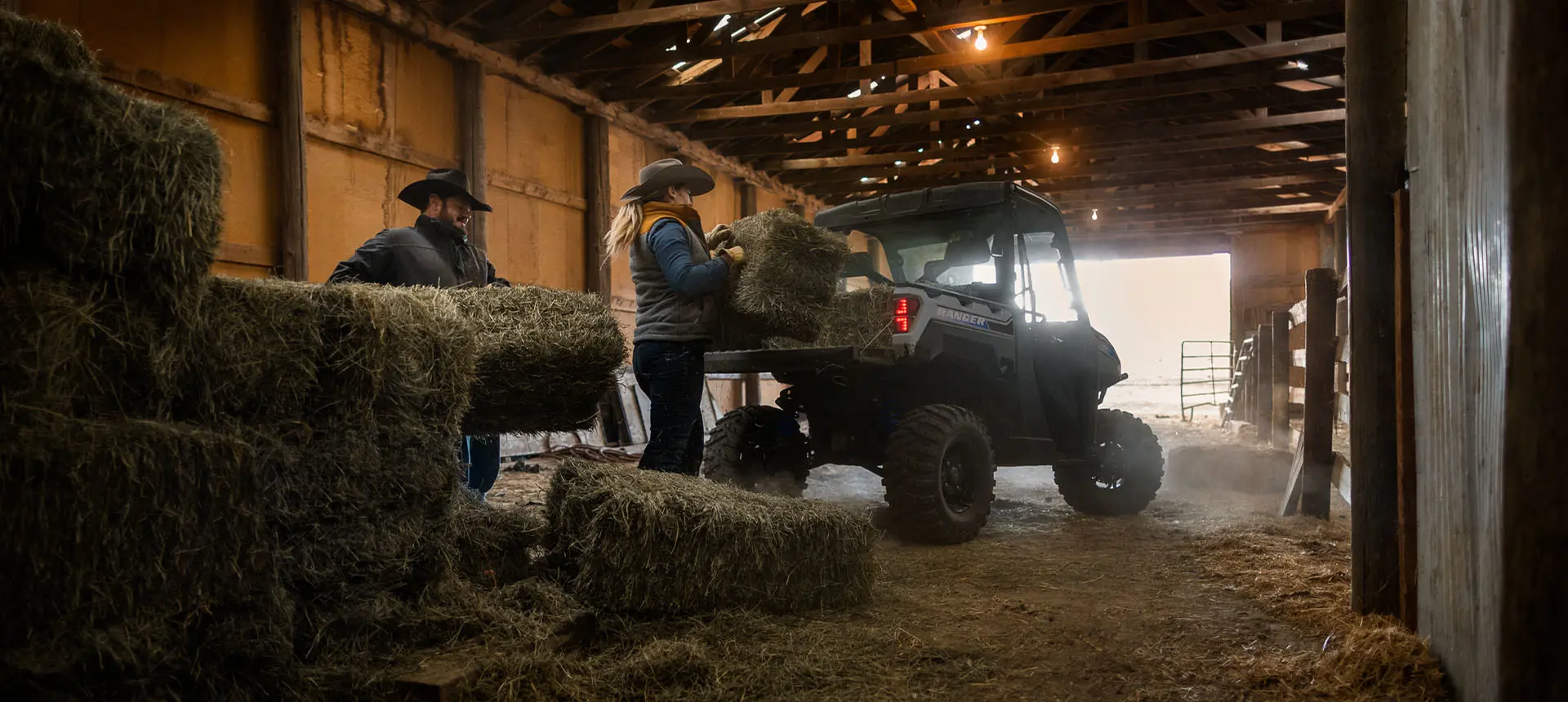 2 farmers loading hay bales into the cargo box of a Polaris RANGER XP Kinetic electric UTV.