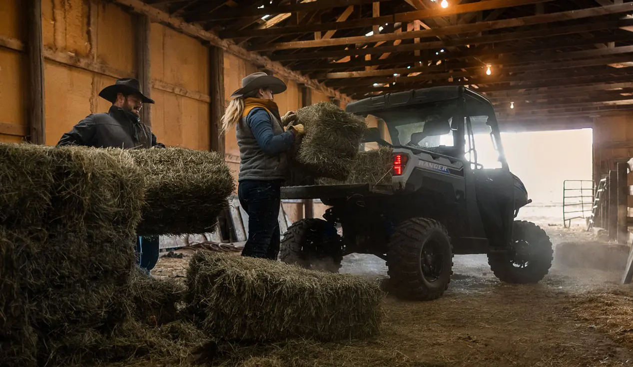 2 farmers loading hay bales into the cargo box of a Polaris RANGER XP Kinetic electric UTV.
