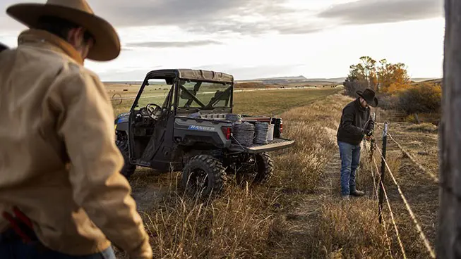 2 ranchers hauling barbed wire in a Polaris RANGER XP Kinetic electric UTV to assist with fence repairs.