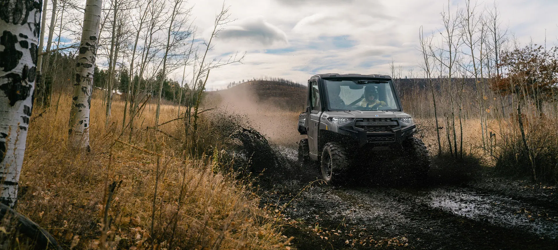 A Polaris RANGER 1000 Cab UTV driving through some mud on a trail.