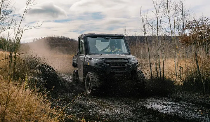 A Polaris RANGER 1000 Cab UTV driving through some mud on a trail.