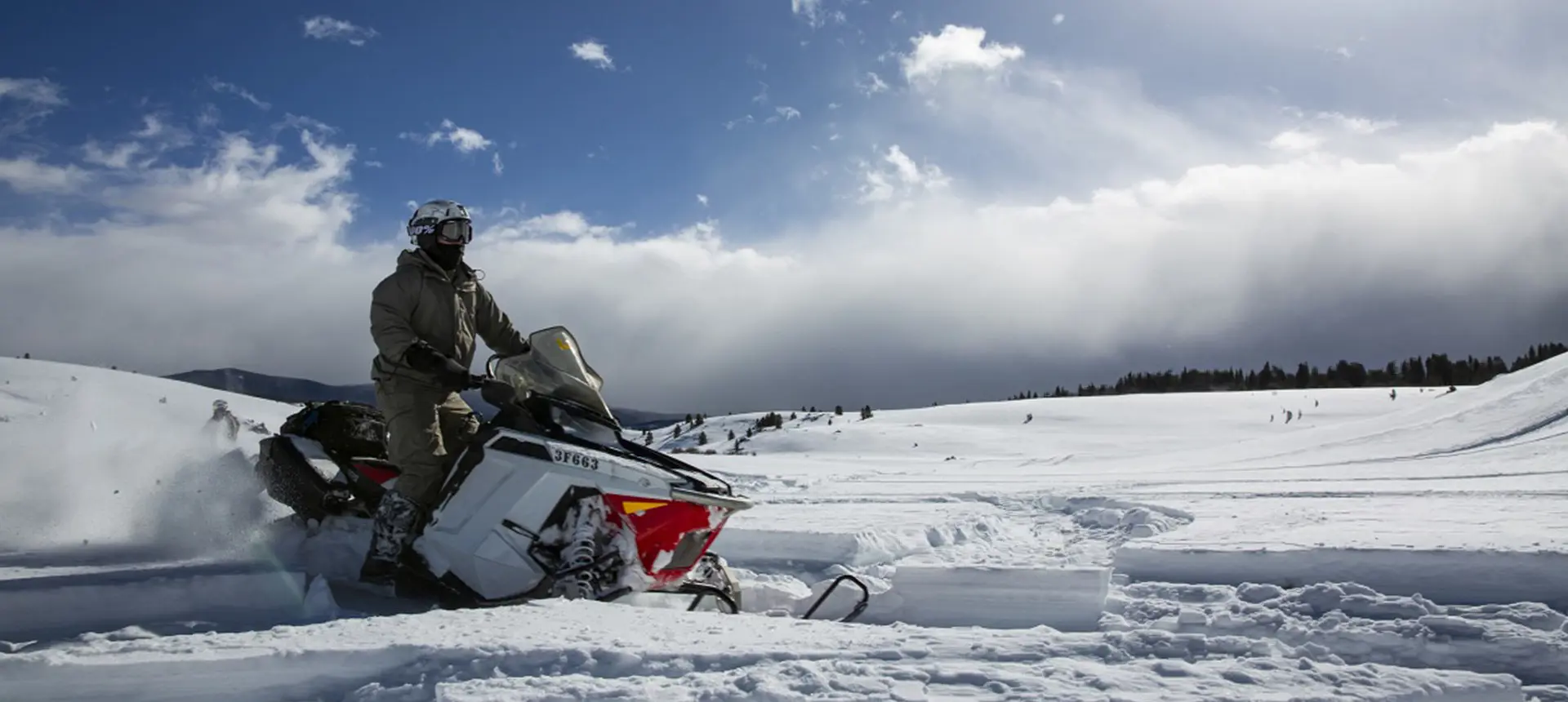 a military pair following a trail on the snow while riding their snowmobiles
