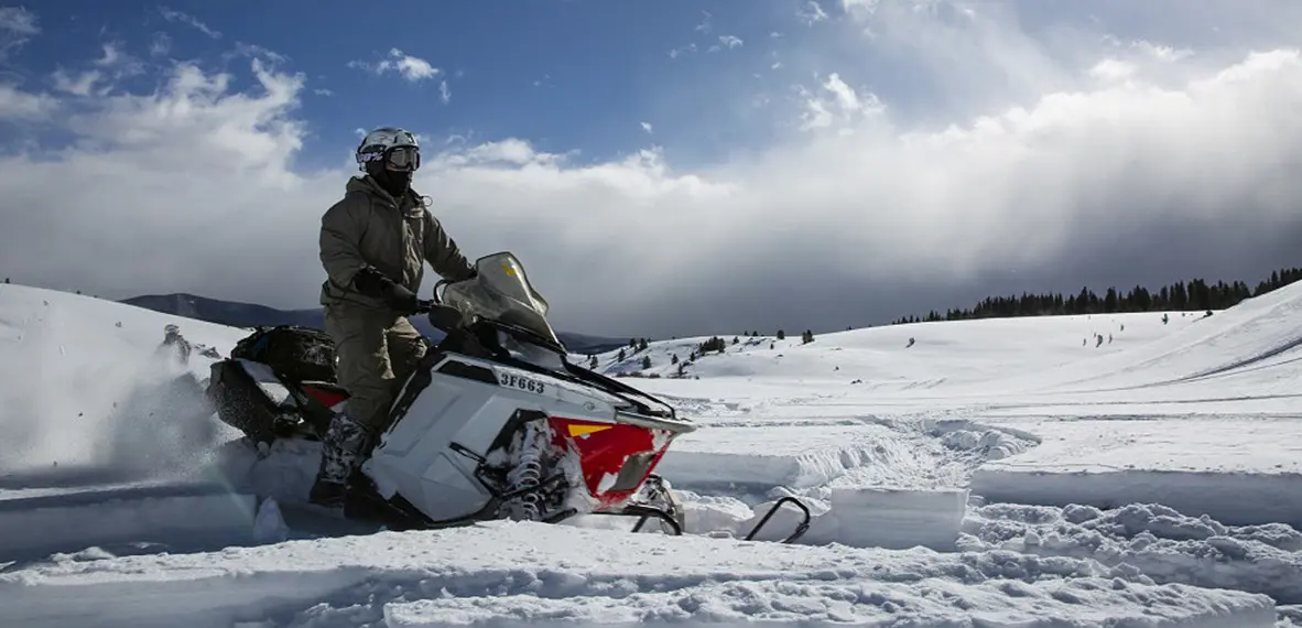 a military pair following a trail on the snow while riding their snowmobiles