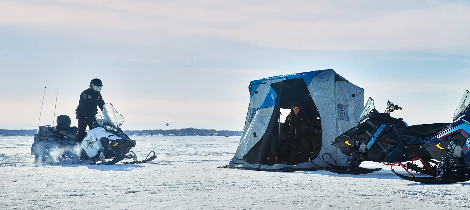 DNR Officer riding on a Polaris Government-issued snowmobile to check on someone ice fishing.