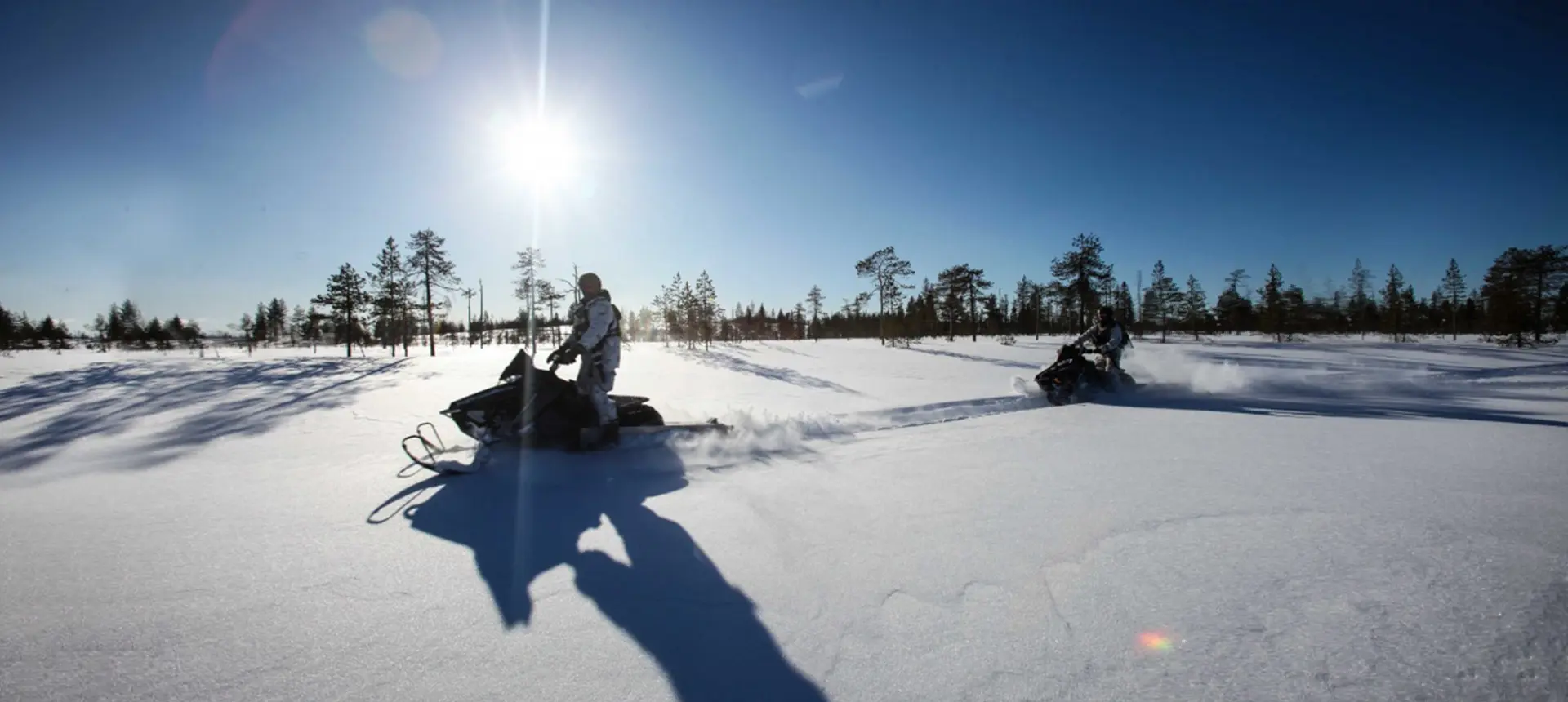 A man his snowmobile through a snowy trail