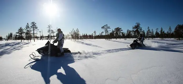 A man his snowmobile through a snowy trail