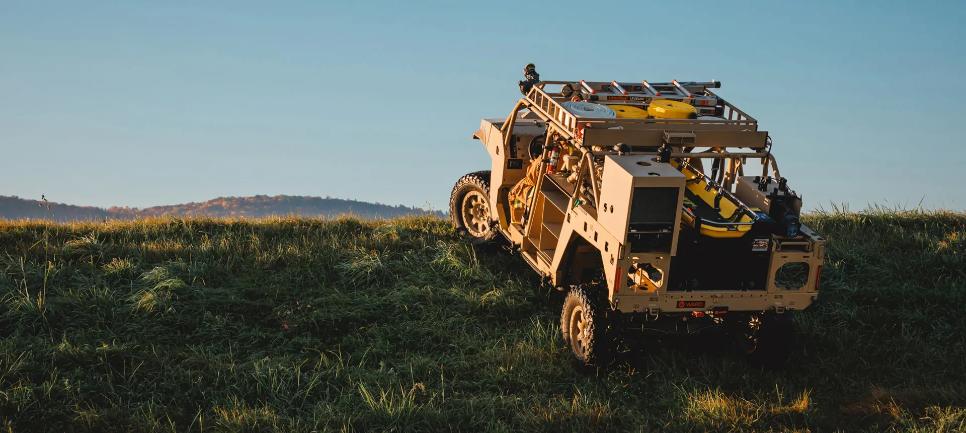 Rear view of a Polaris Government and Defense DAGOR climbing a grassy incline, showcasing its rugged design and externally mounted equipment.
